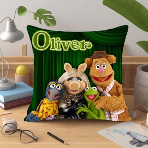 May include: A decorative pillow featuring the Muppets characters: Gonzo, Miss Piggy, Kermit the Frog, and Fozzie Bear. The pillow has a green background with the name "Oliver" in green lettering. The Muppets are in front of a green curtain.