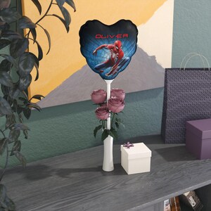 May include: A heart-shaped balloon featuring Spider-Man with the name "OLIVER" in red text. The balloon is held above a bouquet of pink roses in a white vase. A small white gift box with a purple ribbon sits nearby.