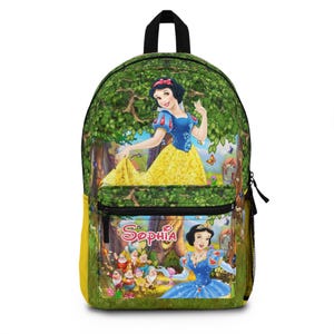 Puede incluir: Una mochila verde con una colorida ilustración de Blancanieves en un entorno forestal. La mochila tiene un asa superior negra, un bolsillo frontal con cremallera y el nombre "Sophia" impreso en la parte delantera. La imagen principal muestra a Blancanieves con un vestido amarillo.