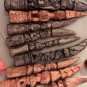 Pode incluir: Uma coleção de dez figuras de madeira esculpidas à mão dispostas em filas. Cada figura apresenta padrões texturizados intrincados e rostos ou formas humanas estilizadas, com vários tons de madeira que variam do castanho claro ao escuro.