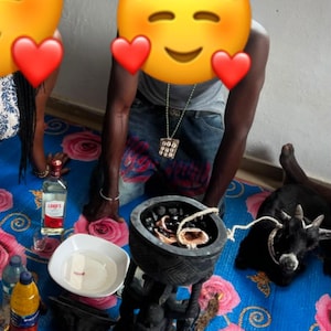 Puede incluir: Un cuenco de madera negra tallada sobre un pedestal que contiene piedras oscuras y una cuerda blanca, colocado sobre una alfombra azul con patrones de rosas rosas. Cerca hay una botella de Lord's Dry Gin, un cuenco blanco con líquido y una cabra.