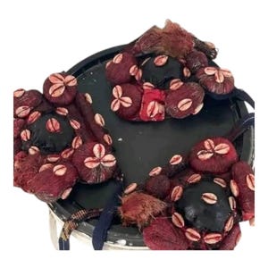Puede incluir: Un tocado decorativo negro adornado con racimos de orbes texturizados de color granate. Cada orbe está adornado con conchas de cauri blancas y beige. El tocado también presenta una franja texturizada de color rojo oscuro y una correa estampada.