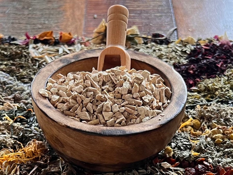 Pode incluir: Uma tigela de madeira cheia de peda&ccedil;os de raiz de bardana secos, de cor castanho claro e irregulares. Uma concha de madeira est&aacute; apoiada na borda da tigela.