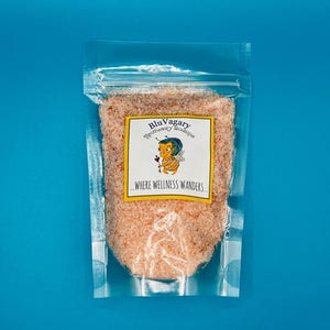 May include: A clear plastic bag filled with pink Himalayan salt. The bag has a label that reads "Blu Vagary Apothecary Boutique...Where Wellness Wanders."