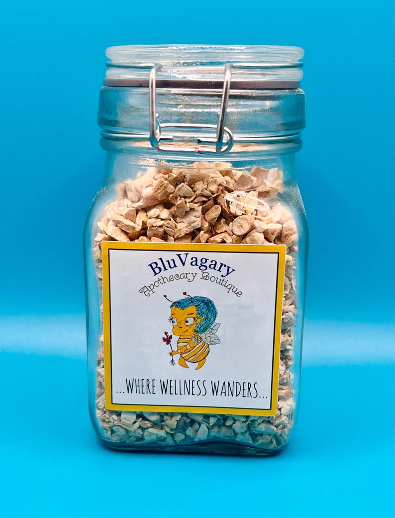 Pode incluir: Um frasco de vidro cheio de peda&ccedil;os secos de raiz de ang&eacute;lica, de cor castanho claro e forma irregular. O frasco tem um fecho de metal e um r&oacute;tulo amarelo com o texto "Blu Vagary Apothecary Boutique...where wellness wanders..." e uma ilustra&ccedil;&atilde;o de abelha de desenho animado.