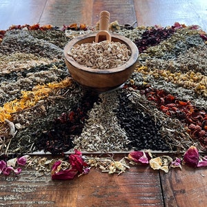 Pode incluir: Uma variedade de ervas e flores secas dispostas em um padr&atilde;o circular sobre uma superf&iacute;cie de madeira. As ervas s&atilde;o de v&aacute;rias cores, incluindo vermelho, laranja, amarelo, verde e marrom. Uma tigela de madeira cheia de ervas secas est&aacute; no centro da disposi&ccedil;&atilde;o.