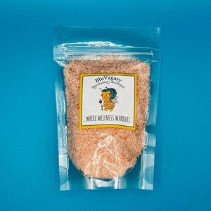 May include: A clear plastic bag filled with pink Himalayan salt. The bag has a label that reads "Blu Vagary Apothecary Boutique...Where Wellness Wanders."