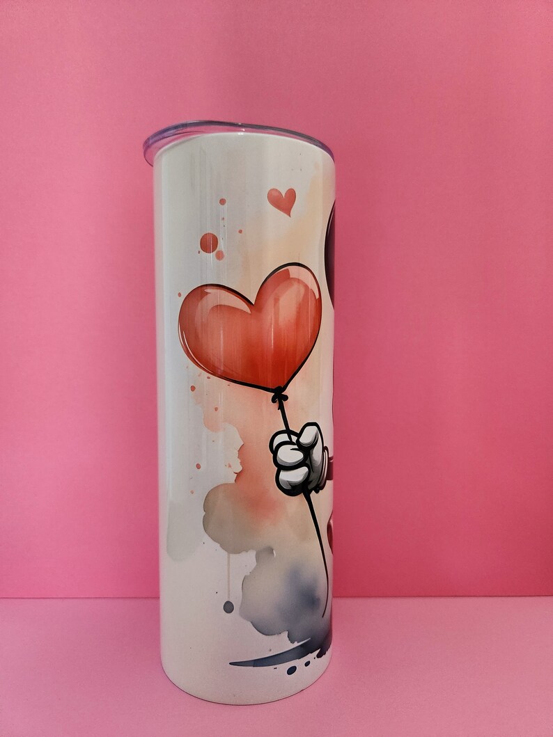 May include: White stainless steel tumbler with a watercolor design of a cartoon character holding a red heart-shaped balloon.
