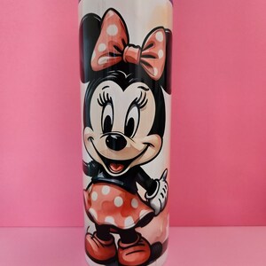 May include: A white stainless steel tumbler with a colorful image of Minnie Mouse. Minnie is wearing a red dress with white polka dots and a red bow.