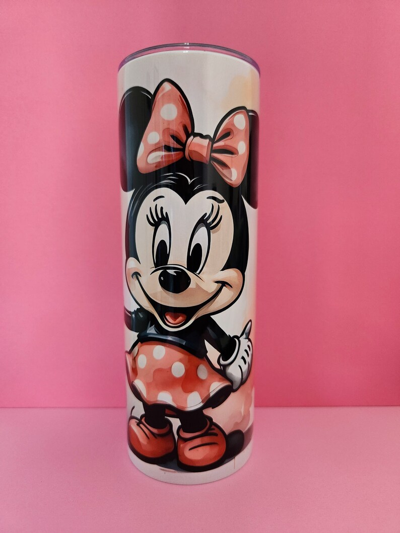 May include: A white stainless steel tumbler with a colorful image of Minnie Mouse. Minnie is wearing a red dress with white polka dots and a red bow.