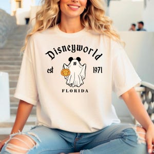 Puede incluir: Camiseta blanca con un gr&aacute;fico negro de un fantasma sosteniendo una calabaza. El texto "Disneyworld est 1971 FLORIDA" est&aacute; impreso en la camiseta.
