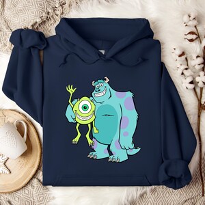 Puede incluir: Sudadera con capucha azul marino con un dibujo animado de Mike Wazowski y James P. Sullivan de la pel&iacute;cula Monstruos S.A. El dibujo muestra a los dos monstruos sonriendo y saludando. La sudadera est&aacute; hecha de un material suave.