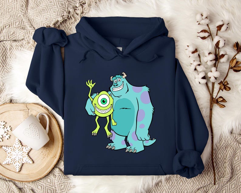 Puede incluir: Sudadera con capucha azul marino con un dibujo animado de Mike Wazowski y James P. Sullivan de la pel&iacute;cula Monstruos S.A. El dibujo muestra a los dos monstruos sonriendo y saludando. La sudadera est&aacute; hecha de un material suave.