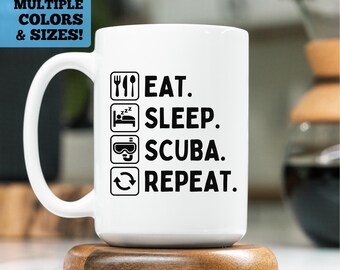 May include: White ceramic mug with the text "EAT. SLEEP. SCUBA. REPEAT." in black. The mug also features icons of a fork and knife, a bed, scuba goggles, and a recycling symbol. The mug is on a wooden coaster.