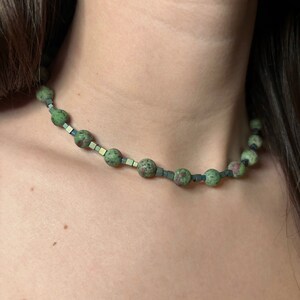 May include: A green and grey gemstone necklace with round beads and square beads.