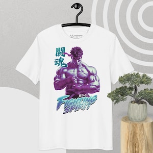 May include: White t-shirt featuring a muscular character illustration in shades of purple and blue. The design includes Japanese text and the words "Fighting Spirit" in a stylized font. The shirt is hanging on a black hanger.
