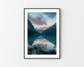May include: A scenic photograph of a mountain lake with a reflection of the mountains and clouds in the water. The lake is surrounded by rocky shores and the mountains are covered in trees.