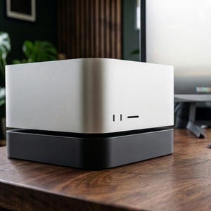 May include: A compact, square-shaped computer tower featuring a two-tone design with a silver metallic upper section and a matte black base. The front panel includes two vertical ports and a horizontal slot, providing a clean and functional aesthetic.