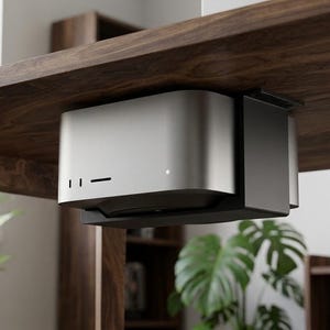 Può includere: Un supporto per computer da sotto scrivania color argento e nero che sostiene saldamente un computer desktop compatto. Il supporto presenta un elegante pannello frontale in metallo argentato con due porte verticali, una fessura e una luce bianca.