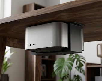 May include: A silver and black under-desk computer mount securely holding a compact desktop computer. The mount features a sleek, metallic silver front panel with two vertical ports and a horizontal slot, alongside a small white indicator light.