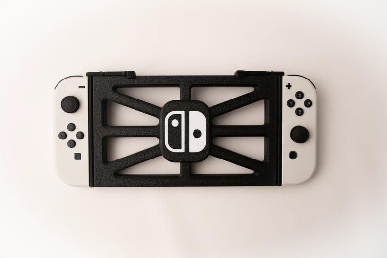 May include: A black and white Nintendo Switch console with a black frame. The frame has a geometric design and surrounds the console's central logo. The controllers are white with black buttons.