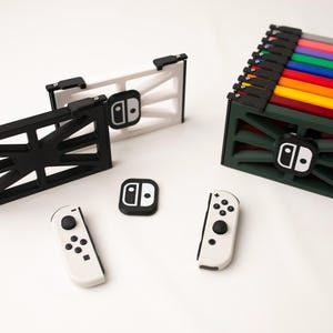 May include: A collection of Nintendo Switch accessories, including a black and white console dock, controller, and a green storage case with colorful game cartridges. The accessories are arranged on a white surface.