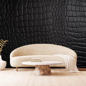 May include: A modern living room scene featuring a cream-colored sofa, a round coffee table with a wood base, and a black textured wall. A white vase with a gold-colored plant and a cream-colored throw blanket add to the decor.