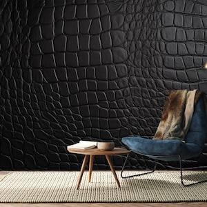 May include: A black crocodile-textured wall covering dominates the scene, complemented by a blue armchair with a brown and beige throw. A small wooden table and a floor lamp add to the room's decor. A neutral-toned rug completes the setting.
