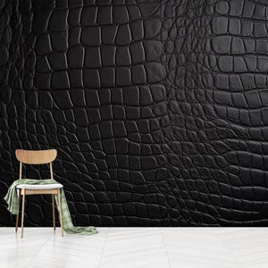 May include: A black textured wall with a crocodile skin pattern. A wooden chair with a green and white scarf draped over it sits in front of the wall. A small plant in a gold vase and a stack of books are on the left.