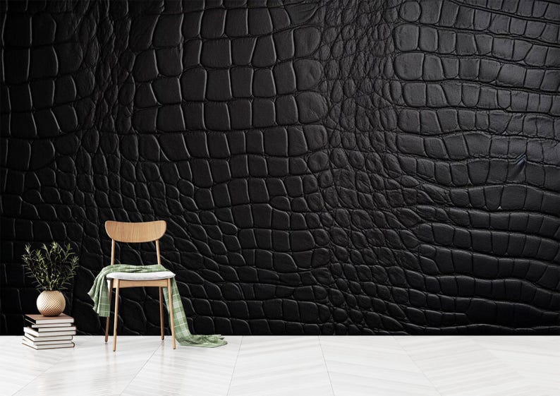 May include: A black textured wall with a crocodile skin pattern. A wooden chair with a green and white scarf draped over it sits in front of the wall. A small plant in a gold vase and a stack of books are on the left.