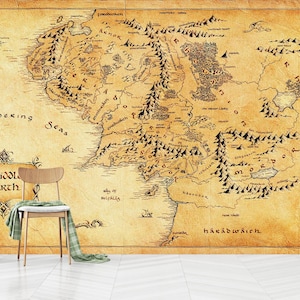 May include: A large, vintage-style map of Middle Earth, with detailed geographical features and text. The map is printed on a textured, aged paper, creating a classic aesthetic. A wooden chair with a green scarf is in front of the map.
