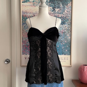 Op de afbeelding: Een zwarte camisole-top met een hartvormige halslijn en dunne spaghettibandjes. Het lijfje is opgebouwd uit zwarte fluwelen en satijnen panelen, met een centraal verticaal paneel van zwart kant over een huidkleurige voering met kleine lovertjes.