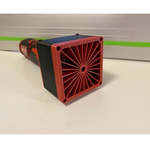 May include: Close-up of a red and black power tool with a red fan vent on the side. The fan vent has a circular opening in the center and is surrounded by a series of red blades.