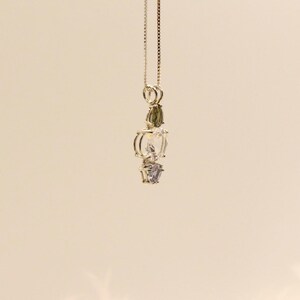 May include: A silver pendant necklace featuring a vertical arrangement of gemstones. The necklace has a delicate chain and showcases a green, clear, and purple gemstone design. The gemstones are faceted and set in a silver metal setting.