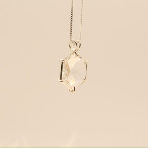 Op de afbeelding: Een zilveren ketting met een heldere, facetgeslepen kristallen hanger. De hanger heeft een geometrische vorm met meerdere zijden en hangt aan een fijne ketting. Het kristal reflecteert het licht, waardoor een sprankelend effect ontstaat. De achtergrond is effen en neutraal.
