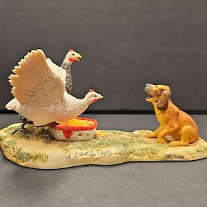 May include: A ceramic figurine of a dog looking at two chickens, one of which is white with its wings spread, and the other is black and white. The chickens are eating from a red and white bowl. The figurine is on a base with the text "vs Lowell Davis" and "122/1250".
