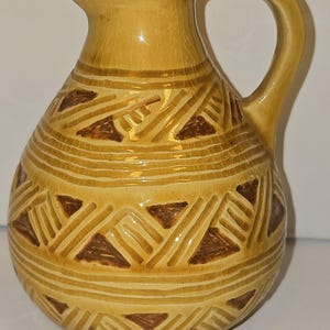 May include: A yellow ceramic pitcher with a brown geometric pattern. The pitcher has a round body and a handle.