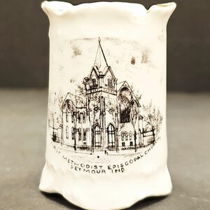 Könnte beinhalten: Weißer Keramik-Fingerhut mit einer Schwarz-Weiß-Illustration der First Methodist Episcopal Church in Seymour, Indiana. Der Fingerhut hat eine gewellte Oberseite und einen ausgestellten Boden.