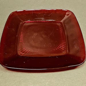 Peut inclure: Un plat carré en verre rouge rubis avec un bord surélevé et une surface légèrement texturée.