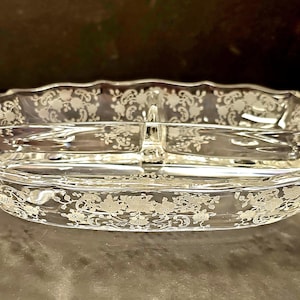 May include: A clear glass serving dish with a divided center and two handles. The dish has a delicate etched floral pattern.
