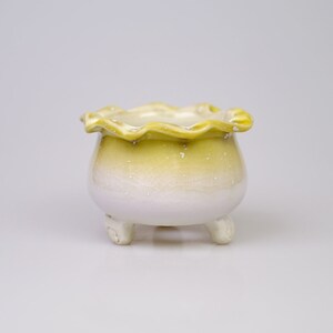 May include: A small, white and yellow ceramic planter with a scalloped rim and three legs.