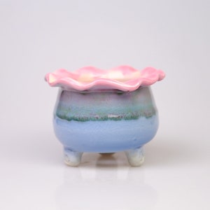 May include: A small, blue and pink ceramic planter with a ruffled rim and three legs.