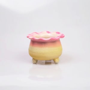 May include: A small, yellow and pink ceramic planter with a scalloped rim and three small feet.