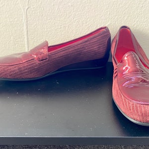 May include: A pair of burgundy suede loafers with a slight wedge heel. One shoe has a patent leather toe.