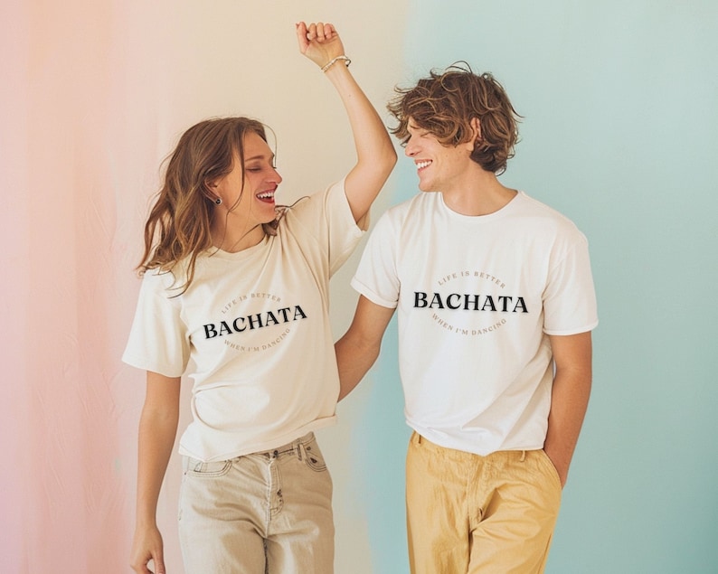 May include: Two people wearing white t-shirts with the text "Life is better when I'm dancing Bachata" printed on them. The people are smiling and dancing.