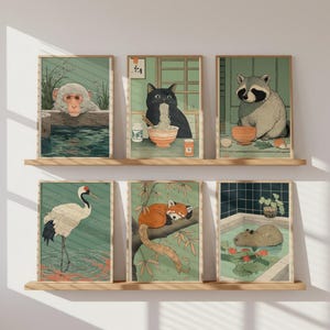 以下が含まれることがあります： 日本のスタイルの、動物が描かれた額入りのアートプリント6枚。温泉に入る猿、ラーメンを食べる猫、アライグマ、鶴、レッサーパンダ、お風呂に入るカピバラが描かれています。各プリントは木製のフレームに入っており、木製の棚に飾られています。