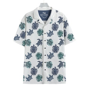 May include: White short-sleeved button-down shirt with a blue and green sea turtle pattern. The shirt has a collar and a pocket on the left chest. The text "KEY LIME SUBlime" is printed on the pocket.