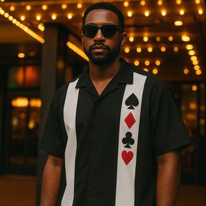 May include: Black button-down shirt with white vertical stripes and playing card suit symbols. The shirt has a classic collar and short sleeves. The word "CASINO" is illuminated in the background.