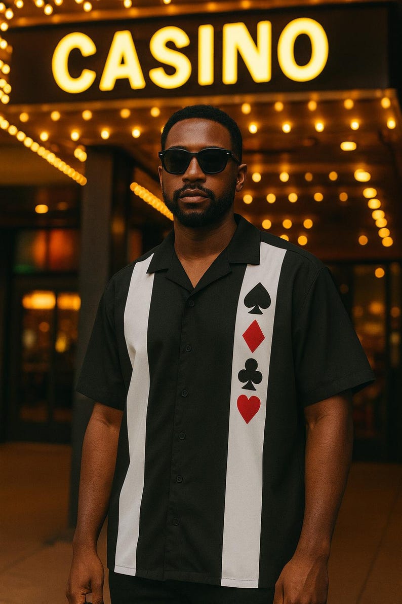 May include: Black button-down shirt with white vertical stripes and playing card suit symbols. The shirt has a classic collar and short sleeves. The word "CASINO" is illuminated in the background.