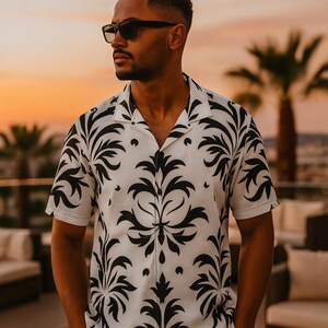 May include: White short-sleeve button-up shirt with a black floral pattern. The shirt has a camp collar and is paired with black sunglasses. The background features a sunset and palm trees.